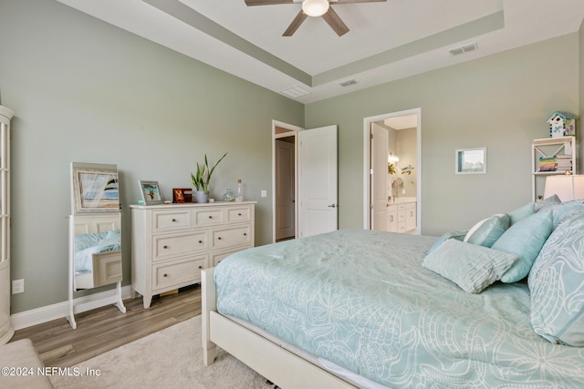 bedroom with connected bathroom, a raised ceiling, ceiling fan, and light wood-type flooring