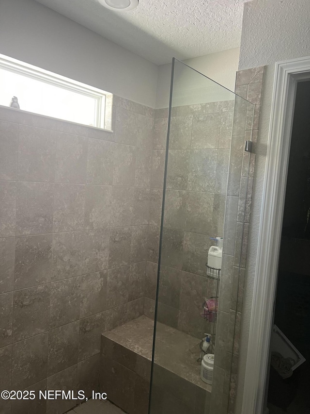 bathroom with tiled shower and a textured ceiling