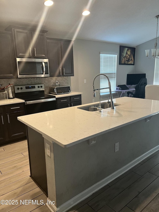 kitchen with pendant lighting, sink, a kitchen island with sink, stainless steel appliances, and light hardwood / wood-style floors