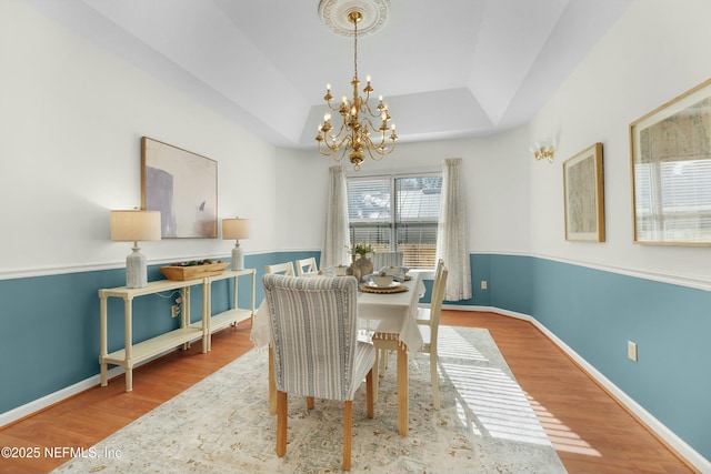 dining space with wood-type flooring, a tray ceiling, and a notable chandelier