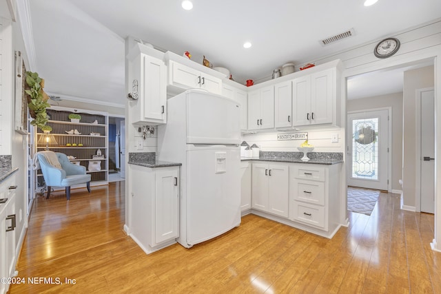 kitchen with white cabinets, dark stone counters, white refrigerator, ornamental molding, and light hardwood / wood-style flooring