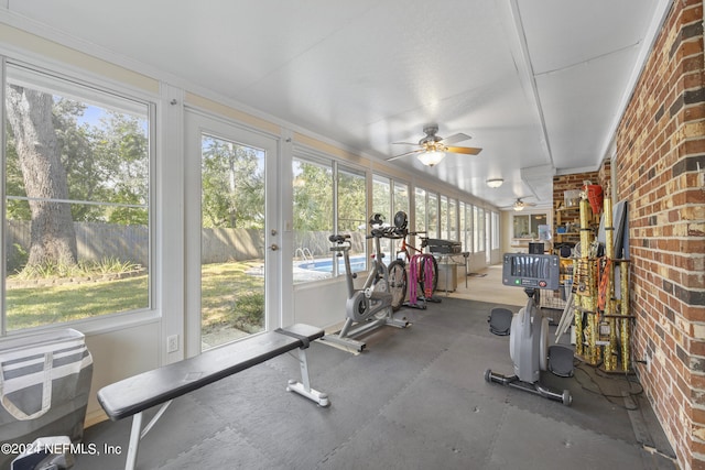 workout area with plenty of natural light, ceiling fan, and brick wall