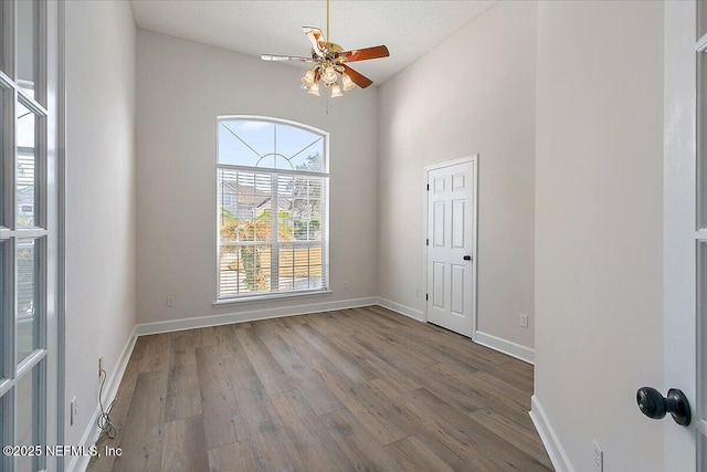 empty room with hardwood / wood-style flooring, ceiling fan, and a high ceiling