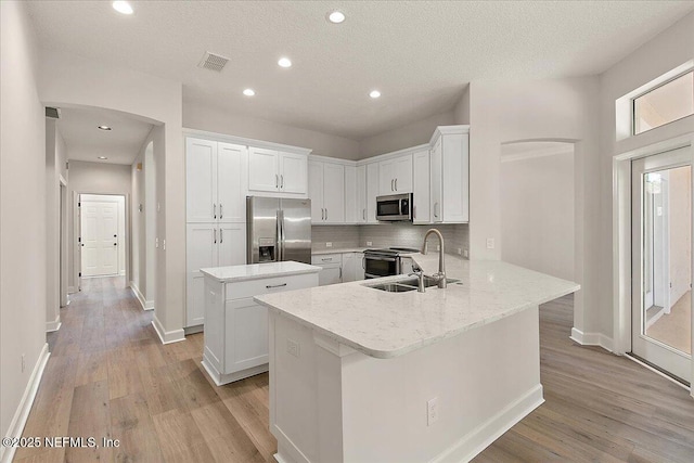 kitchen with sink, appliances with stainless steel finishes, kitchen peninsula, light hardwood / wood-style floors, and white cabinets