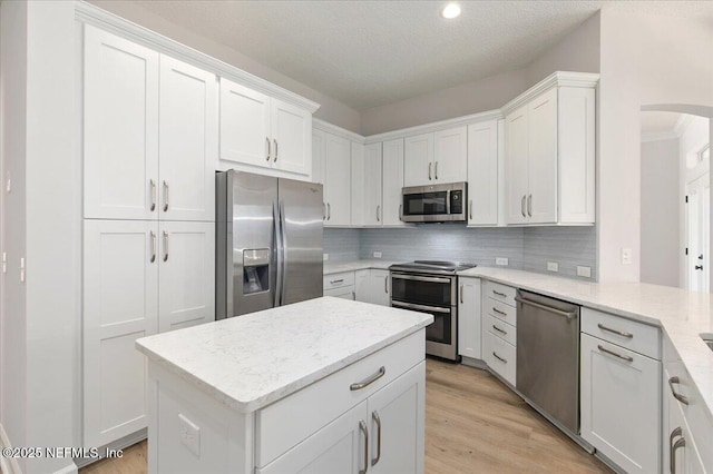 kitchen featuring tasteful backsplash, white cabinetry, light stone counters, stainless steel appliances, and light wood-type flooring