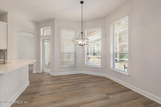 unfurnished dining area with dark hardwood / wood-style floors, sink, a textured ceiling, and a notable chandelier