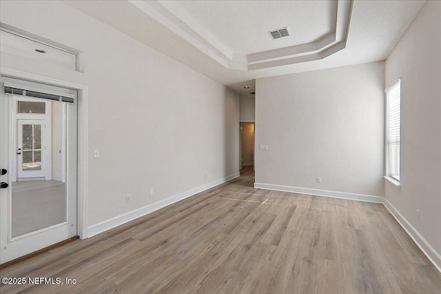 empty room with a raised ceiling, light hardwood / wood-style floors, and a textured ceiling