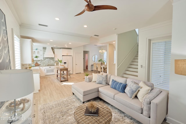 living room with crown molding, ceiling fan with notable chandelier, and light hardwood / wood-style flooring