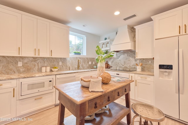 kitchen featuring sink, white cabinets, custom exhaust hood, light stone countertops, and white appliances