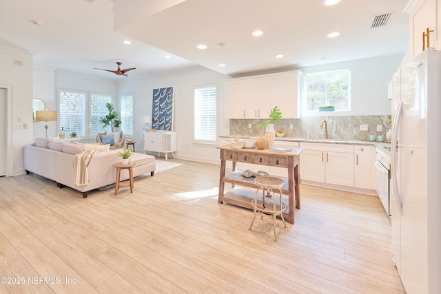 kitchen with tasteful backsplash, light hardwood / wood-style flooring, ornamental molding, white fridge, and white cabinets