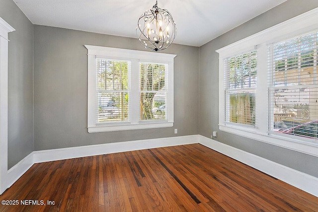 spare room featuring wood-type flooring, a healthy amount of sunlight, and a notable chandelier