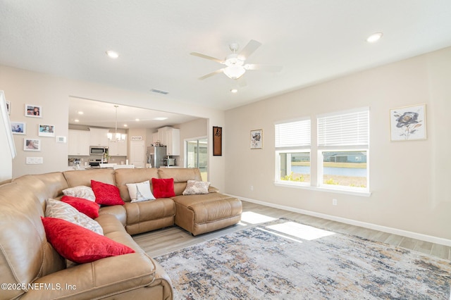 living room featuring ceiling fan with notable chandelier and light wood-type flooring