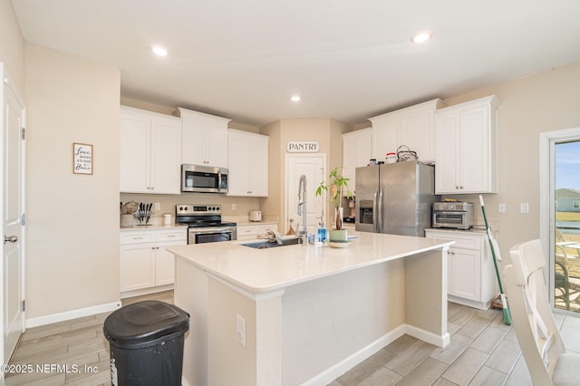 kitchen with white cabinetry, appliances with stainless steel finishes, sink, and a center island with sink