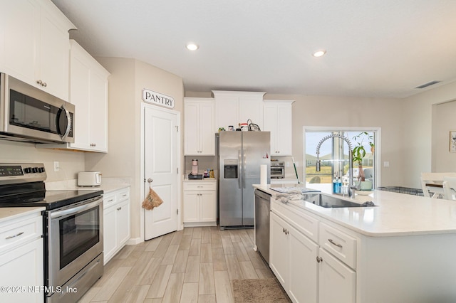 kitchen with stainless steel appliances, sink, a center island with sink, and white cabinets