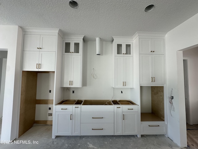 kitchen featuring a textured ceiling, concrete flooring, glass insert cabinets, and white cabinets