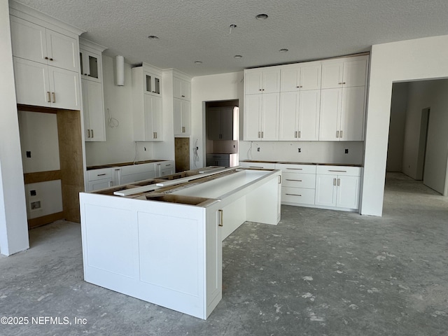 kitchen with a center island, unfinished concrete flooring, glass insert cabinets, white cabinetry, and a textured ceiling