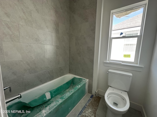 bathroom with toilet, a bathtub, a wealth of natural light, and baseboards