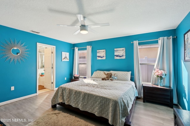 bedroom featuring ceiling fan, ensuite bathroom, light hardwood / wood-style floors, and a textured ceiling