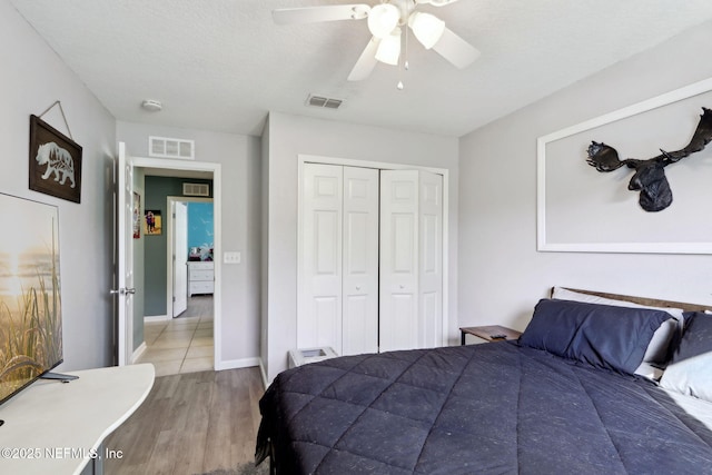 bedroom with ceiling fan, a closet, light hardwood / wood-style flooring, and a textured ceiling