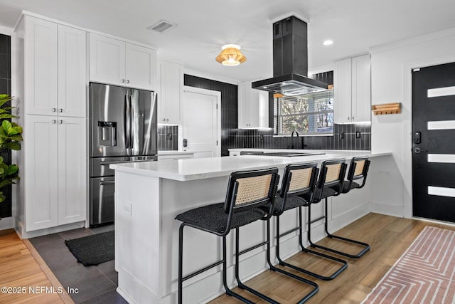 kitchen featuring kitchen peninsula, island range hood, white cabinets, and stainless steel fridge with ice dispenser