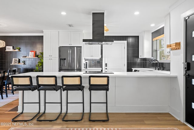 kitchen featuring stainless steel fridge, white cabinetry, a kitchen breakfast bar, island exhaust hood, and kitchen peninsula