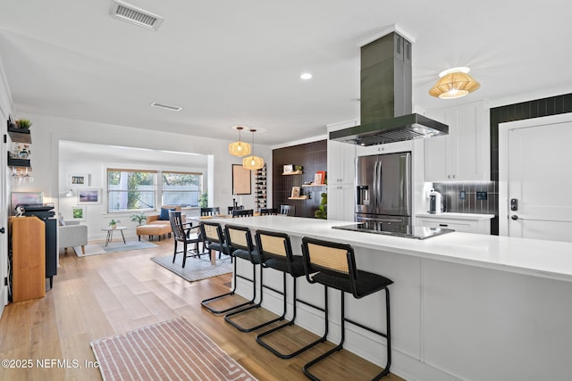 kitchen featuring island range hood, a breakfast bar area, stainless steel fridge, black electric cooktop, and light hardwood / wood-style flooring