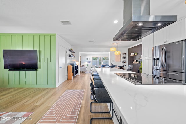 kitchen with stainless steel refrigerator with ice dispenser, pendant lighting, island exhaust hood, light hardwood / wood-style floors, and white cabinets