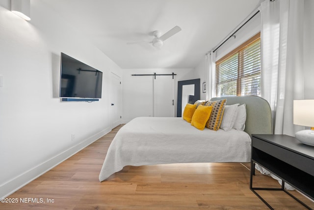 bedroom featuring hardwood / wood-style flooring, ceiling fan, and a barn door