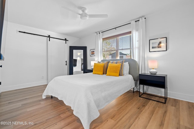 bedroom with ceiling fan, a barn door, and light hardwood / wood-style floors