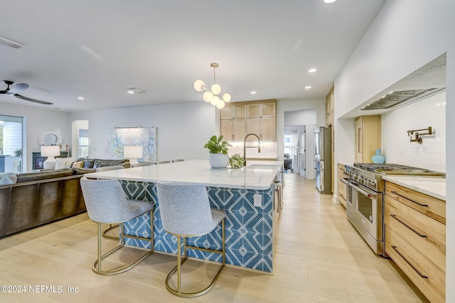 kitchen featuring pendant lighting, sink, stainless steel appliances, a center island with sink, and light brown cabinets