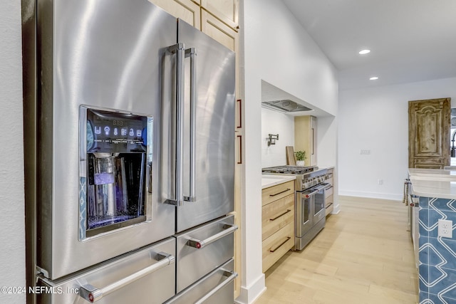 kitchen with high end appliances, wall chimney exhaust hood, light brown cabinetry, and light hardwood / wood-style floors