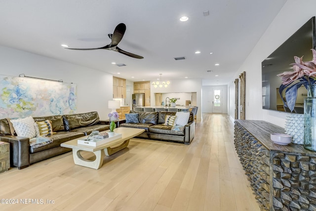 living room with sink, ceiling fan with notable chandelier, and light hardwood / wood-style flooring