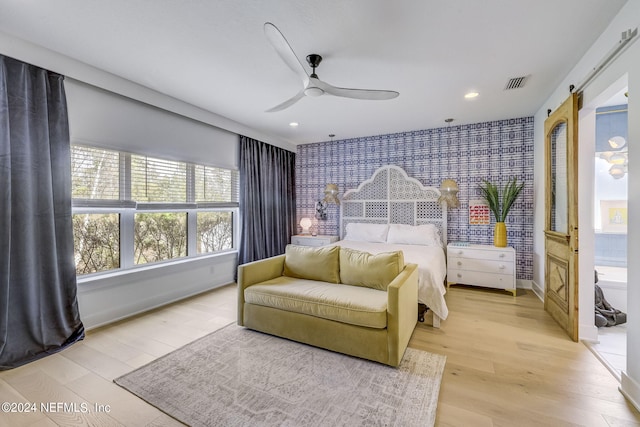 bedroom with ceiling fan, a barn door, and light wood-type flooring