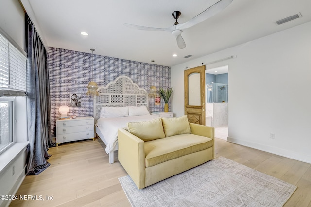 bedroom with ceiling fan, a barn door, light wood-type flooring, and ensuite bath