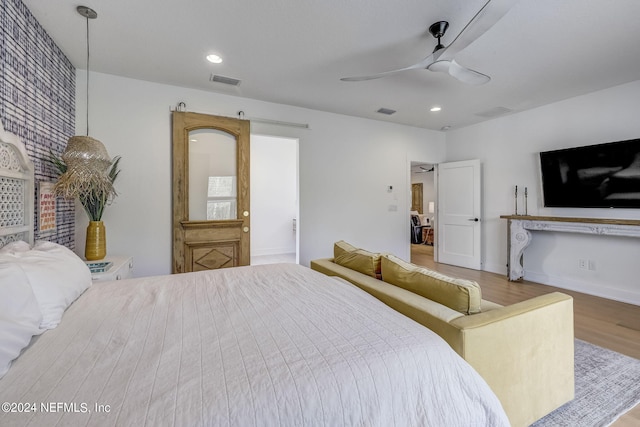 bedroom featuring wood-type flooring, a barn door, and ceiling fan