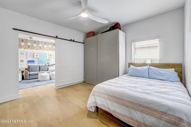 bedroom with light hardwood / wood-style flooring, a barn door, and ceiling fan