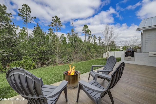 wooden terrace with an outdoor fire pit and a lawn