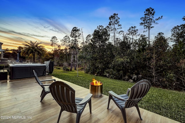 deck at dusk featuring a fire pit, a lawn, and a hot tub