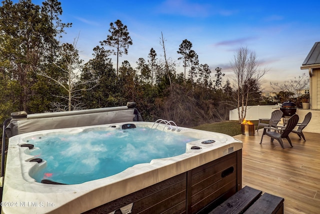 pool at dusk with a wooden deck and a hot tub