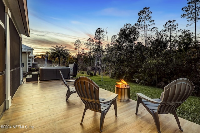 deck at dusk featuring a hot tub and a fire pit