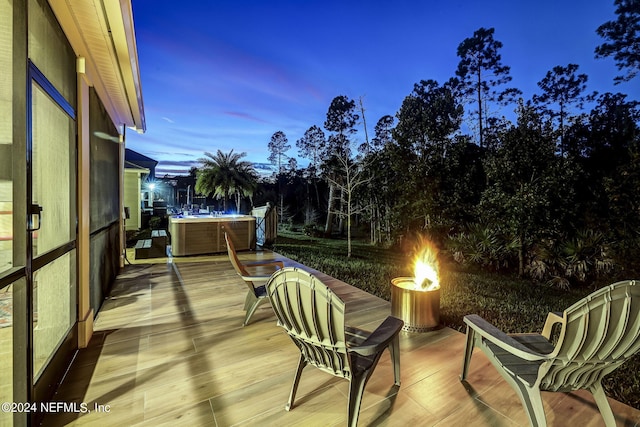 deck at dusk featuring a hot tub and an outdoor fire pit