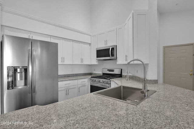 kitchen with sink, light stone counters, appliances with stainless steel finishes, a towering ceiling, and white cabinets