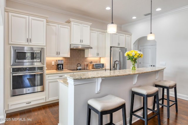 kitchen with hanging light fixtures, light stone countertops, appliances with stainless steel finishes, and a kitchen island with sink