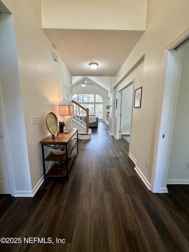 hall with vaulted ceiling, dark hardwood / wood-style floors, and a textured ceiling