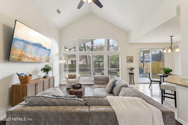 living room with ceiling fan with notable chandelier, high vaulted ceiling, and light tile patterned floors