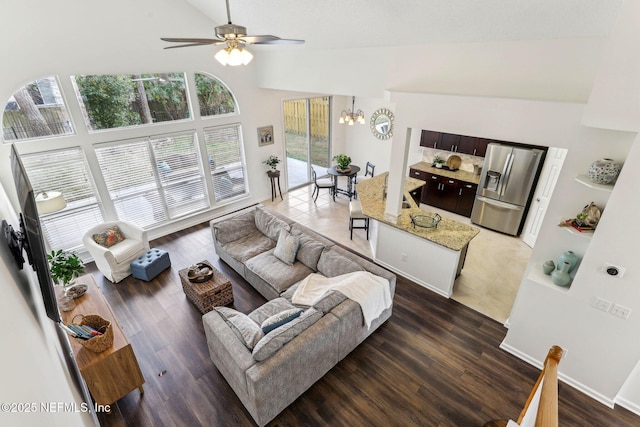 living room featuring dark wood-type flooring, ceiling fan with notable chandelier, and high vaulted ceiling