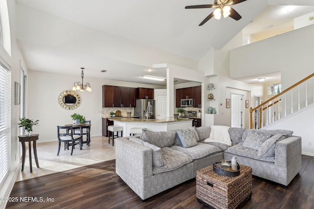 living room featuring dark hardwood / wood-style flooring, ceiling fan with notable chandelier, and high vaulted ceiling