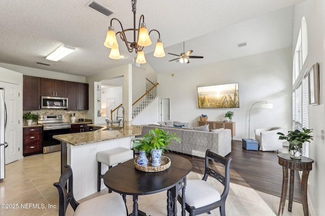 dining room with lofted ceiling, sink, a textured ceiling, light tile patterned floors, and ceiling fan with notable chandelier