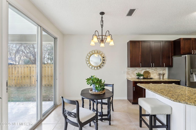 kitchen with decorative light fixtures, stainless steel fridge, decorative backsplash, light tile patterned floors, and light stone counters