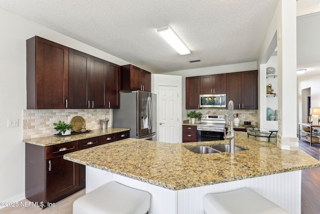 kitchen with light stone counters, stainless steel appliances, a kitchen breakfast bar, and kitchen peninsula